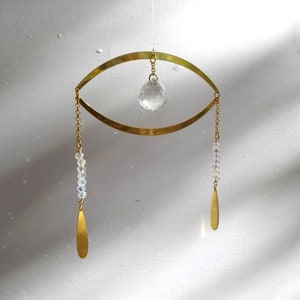 May include: Gold eye-shaped metal mobile with a crystal ball hanging from the centre and two crystal strands hanging from the sides, each ending with a gold teardrop.