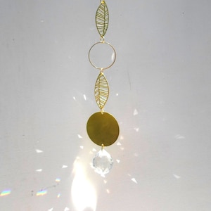 以下が含まれることがあります： 下部にクリスタルプリズムがぶら下がった金色の金属製のサンキャッチャー。サンキャッチャーは円形、葉の形が3つ、大きな丸い円盤が特徴です。