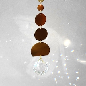 Op de afbeelding: Een gouden metalen zonenvanger met een kristallen prisma dat aan de onderkant hangt. De zonenvanger heeft een reeks aflopende cirkels, waarbij de grootste cirkel onderaan en de kleinste bovenaan is.