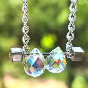 May include: A silver chain necklace with two clear crystal teardrop pendants and silver cube accents.