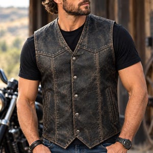 May include: A distressed black leather waistcoat featuring a V-neckline, five silver-toned metal buttons down the front, and two vertical side pockets. The waistcoat has a weathered, worn-in texture with visible brown undertones throughout the leather surface.