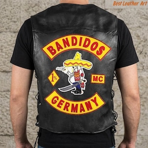 May include: A black leather vest featuring a large embroidered patch on the back. The patch displays the text BANDIDOS in red on a yellow arc, a cartoon figure wearing a sombrero holding a gun and sword, a 1% diamond, MC text, and GERMANY.