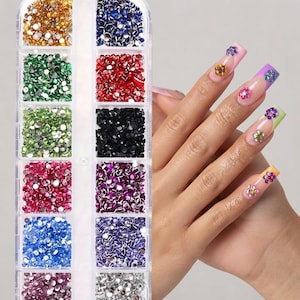 May include: A clear plastic rectangular storage container with twelve individual compartments filled with small, round, multi-coloured rhinestones. The rhinestones are arranged by colour, including gold, blue, green, red, black, pink, and silver.