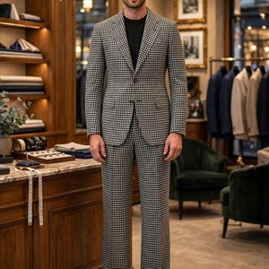 May include: A two-piece suit featuring a black and white houndstooth pattern, consisting of a single-breasted blazer with notched lapels and matching trousers, worn over a solid black crew-neck shirt in a professional tailoring environment.