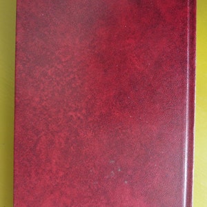 K&ouml;nnte beinhalten: Ein tief rotes, ledergebundenes Buch mit einem strukturierten Einband.