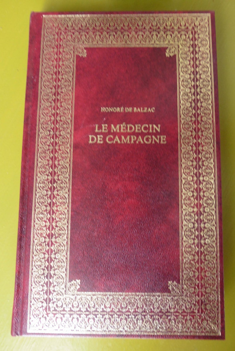 K&ouml;nnte beinhalten: Ein rotes, ledergebundenes Buch mit goldenen Verzierungen und dem Titel "HONORE DE BALZAC LE MEDECIN DE CAMPAGNE" auf dem Einband.