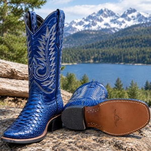 Könnte beinhalten: Ein Paar leuchtend blaue Cowboystiefel mit strukturiertem, schlangenlederartigem Vorderblatt und einem hohen Schaft mit aufwendigen silbernen Stickereien. Ein Stiefel steht aufrecht, der andere liegt seitlich und zeigt eine hellbraune Ledersohle.