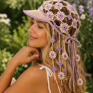 May include: A crochet baseball cap featuring a lavender and cream floral pattern with dangling flower motifs and gold-toned beads. The cap has a solid lavender brim and long crocheted ties at the back, creating a detailed, textured headwear piece.