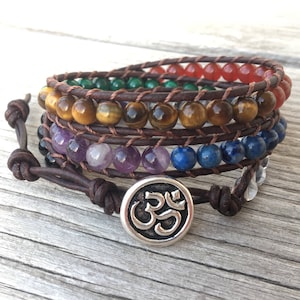 May include: A brown leather wrap bracelet with seven chakra stones, including tiger's eye, amethyst, lapis lazuli, and clear quartz. The bracelet features a silver Om charm.