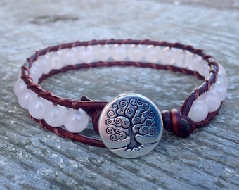 May include: A brown leather wrap bracelet with a silver tree of life charm and white beads.