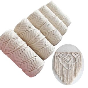 May include: Four cylindrical spools of off-white cotton cord arranged diagonally, accompanied by a circular inset showing a wall hanging made from the same cord, featuring intricate knotted patterns and long, straight fringe.