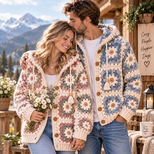 Può includere: Due cardigan con cappuccio realizzati in piastrelle di uncinetto con motivo a margherita. Uno presenta toni crema, rosa e verde salvia, mentre l'altro mostra colori crema, blu e marrone chiaro. Entrambi sono dotati di bottoni in legno e nappe.