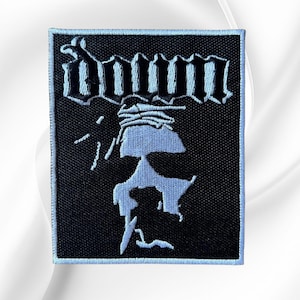 May include: A rectangular embroidered patch featuring a black background with white stitching. The word "down" is written in a stylized gothic font at the top, positioned above a white abstract graphic design that resembles a crown of thorns.