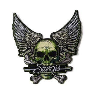 May include: An embroidered patch featuring a green skull with large, detailed grey wings extending upwards. Crossed grey bones are positioned behind the skull, and a black horizontal banner with the white text Sturgis is centered.