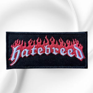 May include: A rectangular embroidered patch with a black background. The word "hatebreed" is stitched in light blue lettering across the center, positioned beneath a stylized row of red flames that span the width of the patch.
