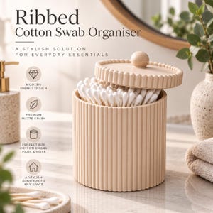 May include: A cylindrical beige cotton swab organiser with a vertical ribbed texture and a matching lid featuring a small spherical knob. The container is filled with white cotton swabs. Text on the image reads Ribbed Cotton Swab Organiser.