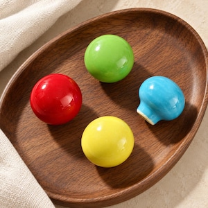 May include: Four smooth, spherical cabinet knobs in glossy red, bright green, sunny yellow, and sky blue. Each knob features a polished, reflective surface and a rounded shape, designed for attachment to furniture drawers or cabinet doors.