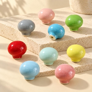 Puede incluir: Un conjunto de nueve pomos de cerámica para armarios, lisos y redondos, en varios colores brillantes que incluyen rosa, gris, verde, azul intenso, rojo, azul claro, amarillo y verde menta, cada uno con un orificio central de metal.