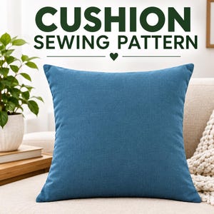 May include: A square blue cushion with a textured fabric finish. The text CUSHION SEWING PATTERN is printed in dark green above the cushion, separated by a small heart icon. The cushion is positioned in a room setting with a plant and a sofa.