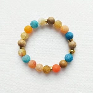 Può includere: Un braccialetto di perline colorate con un mix di perline blu, arancioni e marroni. Il braccialetto è realizzato con perline di agata e legno.