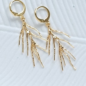 May include: A pair of gold earrings with a delicate, branch-like design. The earrings are made of thin, textured metal and have a hoop closure.