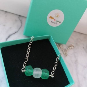 Peut inclure: Un collier en cha&icirc;ne argent&eacute;e avec trois perles en verre de mer. Les perles sont vertes et blanches. Le collier est dans une bo&icirc;te turquoise avec le texte "Sun & Soul Jewels".
