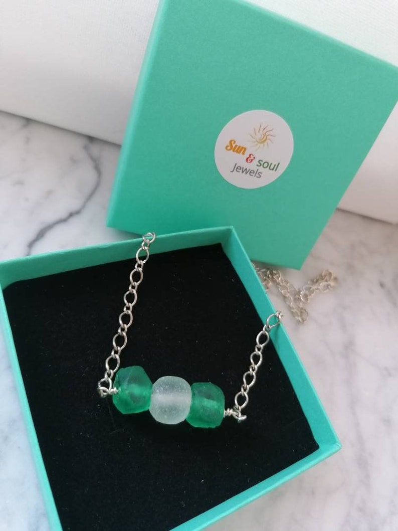 Peut inclure: Un collier en cha&icirc;ne argent&eacute;e avec trois perles en verre de mer. Les perles sont vertes et blanches. Le collier est dans une bo&icirc;te turquoise avec le texte "Sun & Soul Jewels".