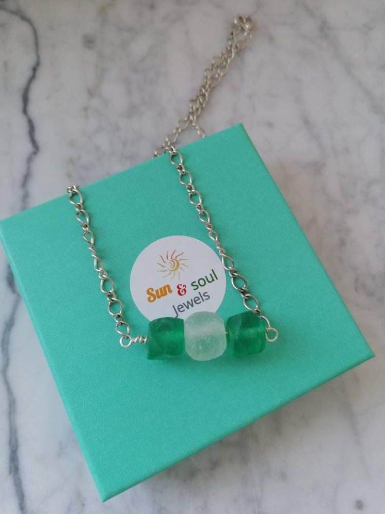 Peut inclure: Un collier en cha&icirc;ne argent&eacute;e avec trois perles&nbsp;: deux perles en verre vert et une perle en verre blanc. Le collier est dans une bo&icirc;te cadeau turquoise avec une &eacute;tiquette blanche qui dit&nbsp;&laquo;&nbsp;Sun & Soul Jewels&nbsp;&raquo;.