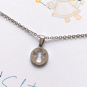 May include: A silver necklace with a round pendant featuring a cutout angel design. The pendant is hanging from a silver chain. The necklace is displayed on a white card with the text "Schutzengel f&uuml;r" in blue.