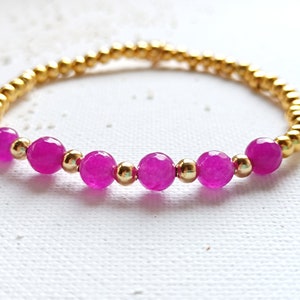 May include: A gold beaded bracelet with pink gemstone beads. The bracelet is made with small gold beads and larger pink beads.