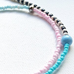 May include: A multi-colored beaded bracelet with pink, blue, black, and white beads. The bracelet has a silver bead accent.