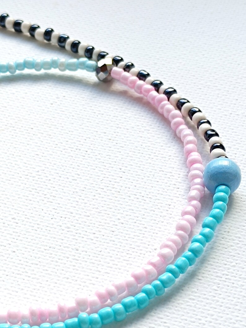 May include: A multi-colored beaded bracelet with pink, blue, black, and white beads. The bracelet has a silver bead accent.