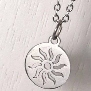 May include: A silver necklace with a circular pendant featuring a cut-out design of a sun with rays.