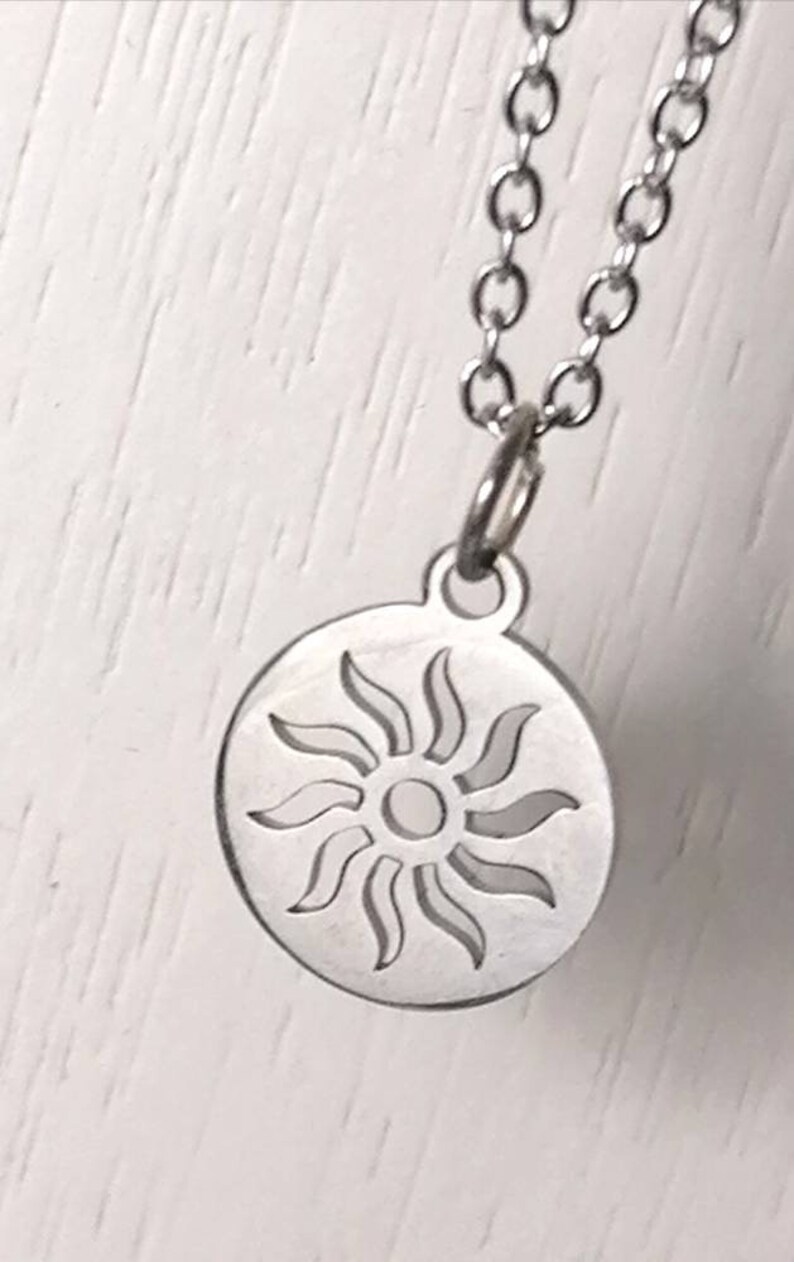 May include: A silver necklace with a circular pendant featuring a cut-out design of a sun with rays.