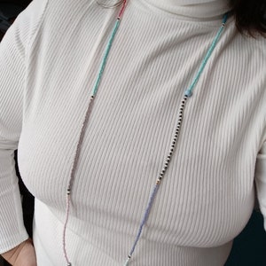 May include: A white turtleneck sweater with a multi-colored beaded necklace. The necklace has pink, blue, and black beads.