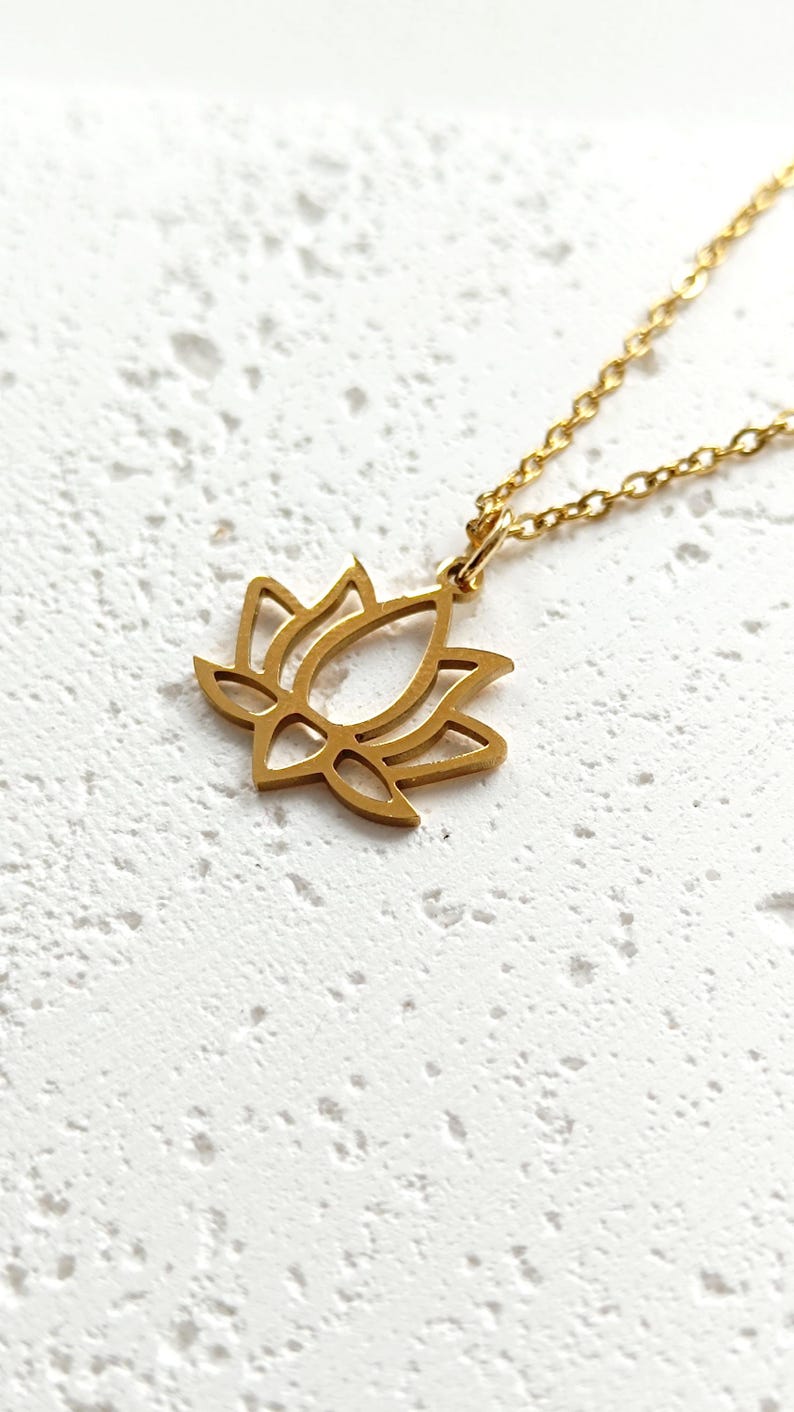 May include: A gold-toned necklace with a delicate lotus flower pendant. The pendant is a simple outline of a lotus flower.