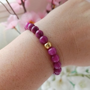 May include: A purple gemstone bracelet with gold beads. The bracelet is on a person's wrist.
