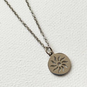 May include: A silver chain necklace with a circular pendant featuring a cut-out sun design.