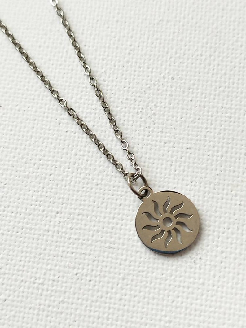 May include: A silver chain necklace with a circular pendant featuring a cut-out sun design.