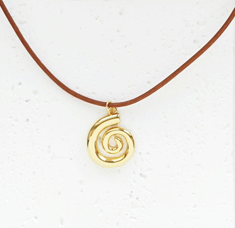 May include: A gold-coloured spiral pendant necklace with a brown cord. The pendant is a stylized spiral design, suspended from a delicate gold-toned bail. The cord is a thin, smooth, and brown.