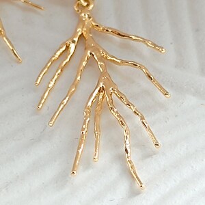 May include: Gold earrings with a delicate, branch-like design. The earrings are made of a textured metal and have a simple hoop closure.
