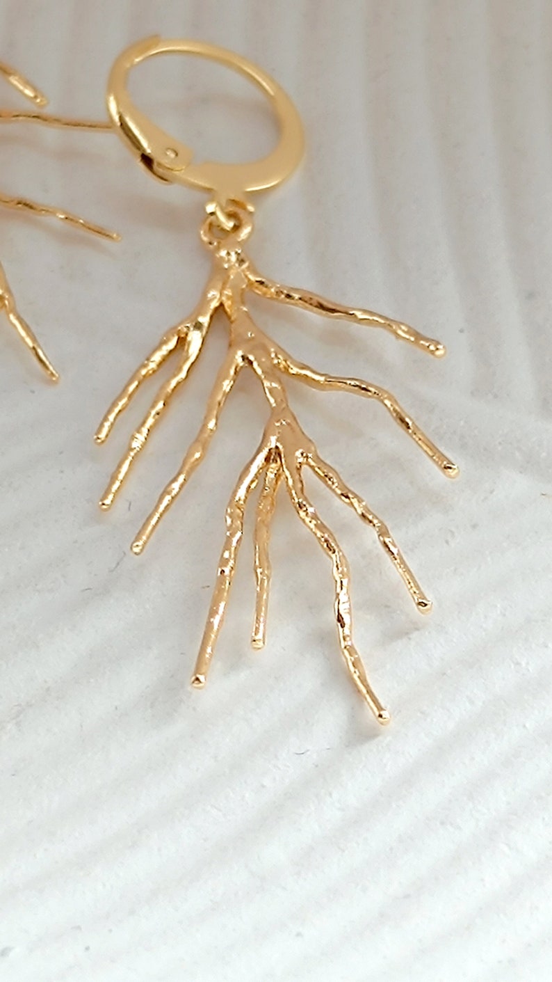 May include: Gold earrings with a delicate, branch-like design. The earrings are made of a textured metal and have a simple hoop closure.