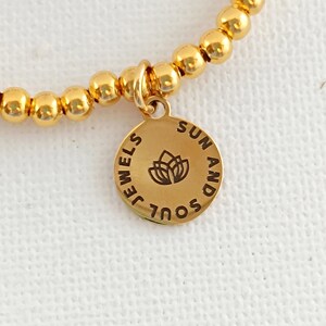 May include: Gold beaded bracelet with a charm that says "Soul and Sun" with a flower design.
