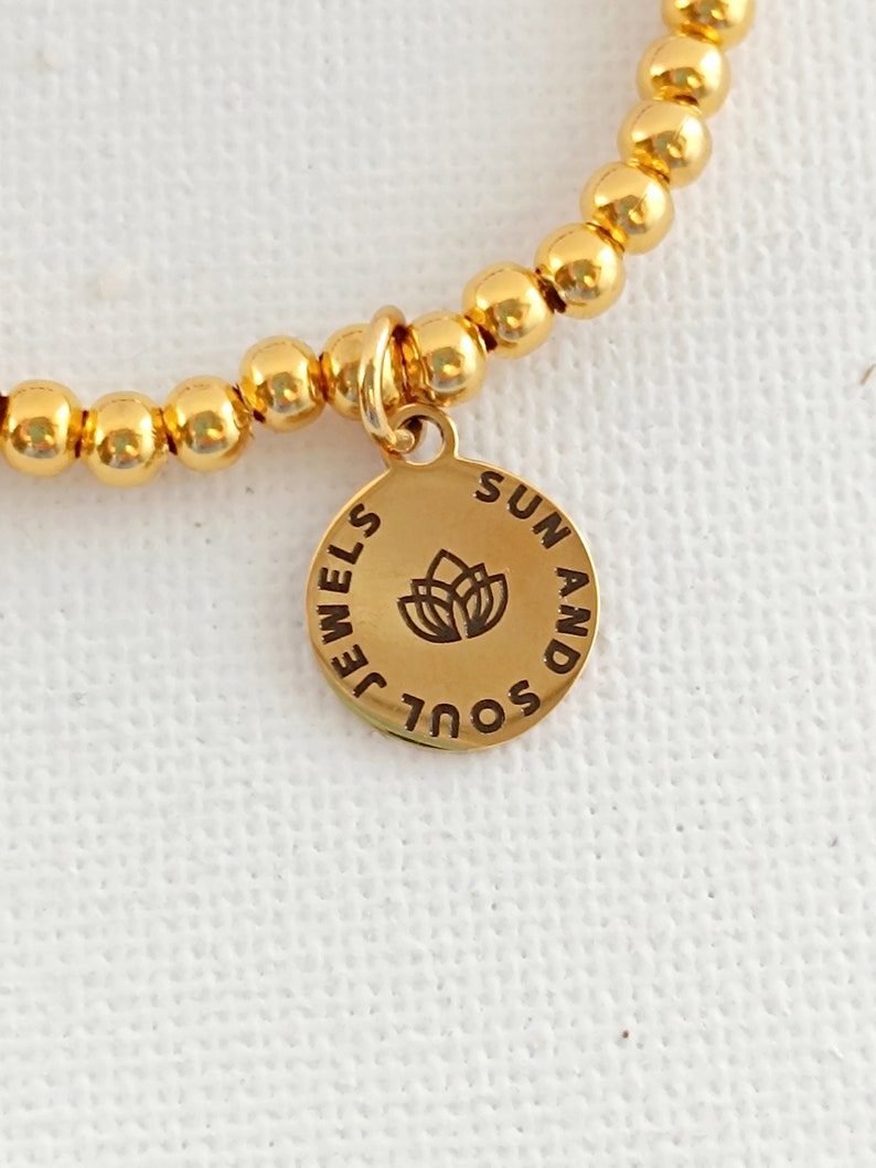 May include: Gold beaded bracelet with a charm that says "Soul and Sun" with a flower design.