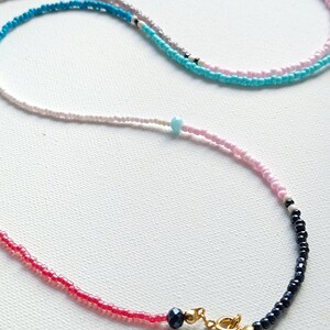 May include: A layered necklace with pink, white, blue, and black beads. The necklace has a gold clasp.