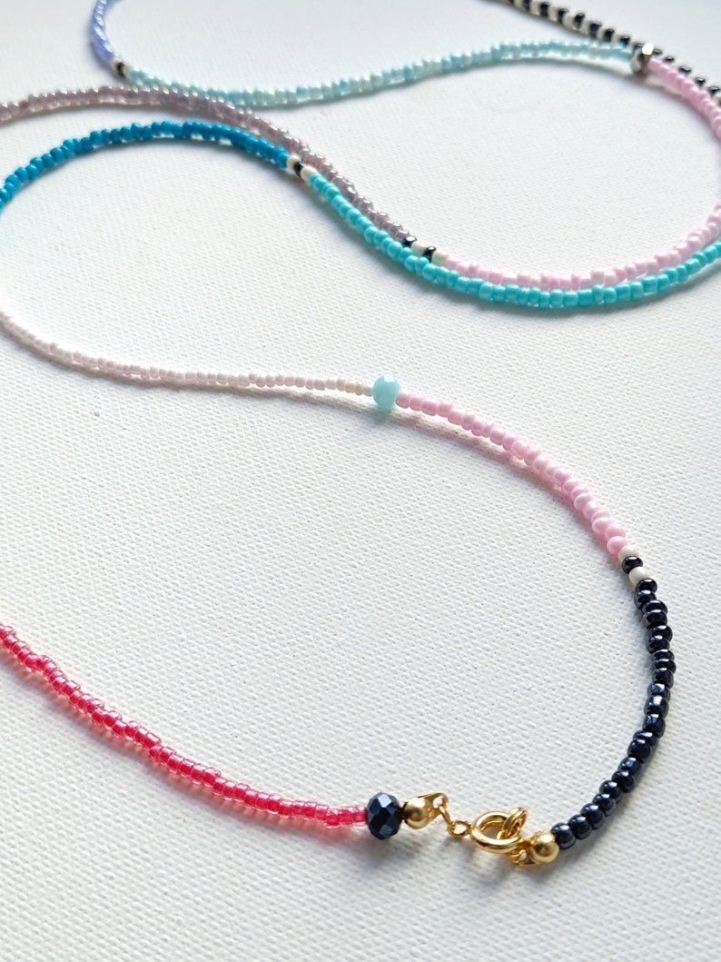 May include: A layered necklace with pink, white, blue, and black beads. The necklace has a gold clasp.