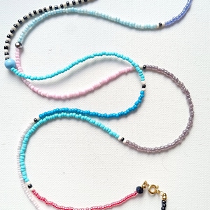May include: A layered beaded necklace with a variety of colors, including black, white, light blue, turquoise, pink, and red. The necklace has a gold clasp.