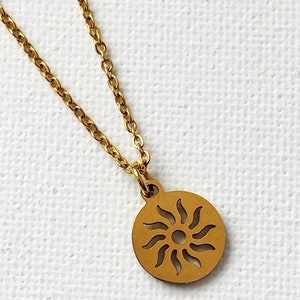 May include: A gold chain necklace with a circular pendant featuring a sun design with rays.