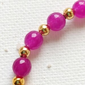 May include: A close-up of a pink and gold beaded bracelet. The bracelet is made with small, round gold beads and larger, faceted pink beads.