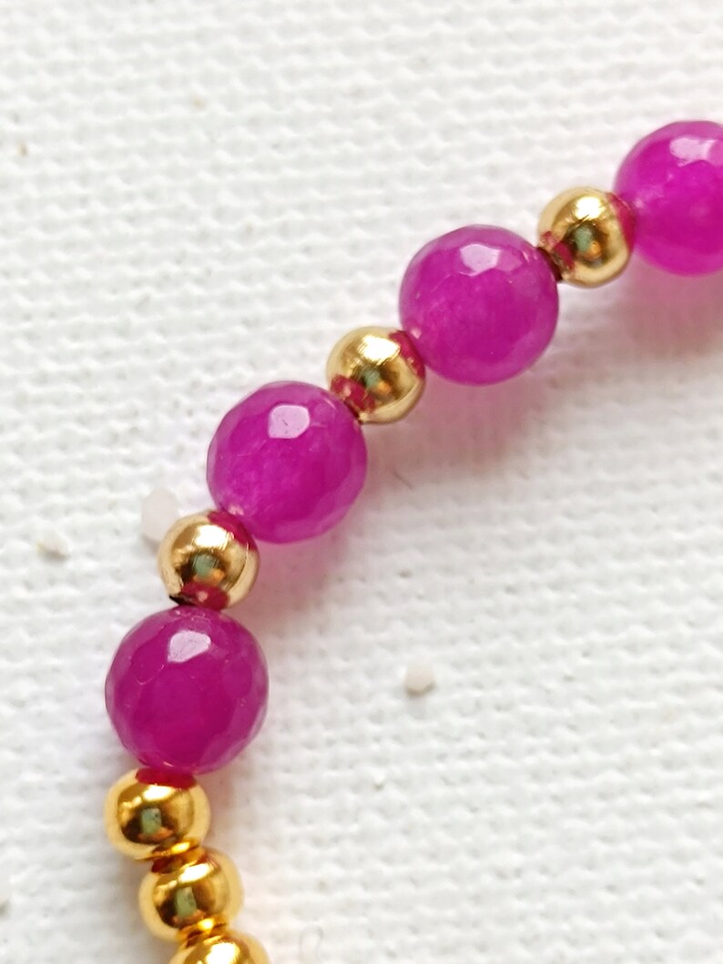 May include: A close-up of a pink and gold beaded bracelet. The bracelet is made with small, round gold beads and larger, faceted pink beads.